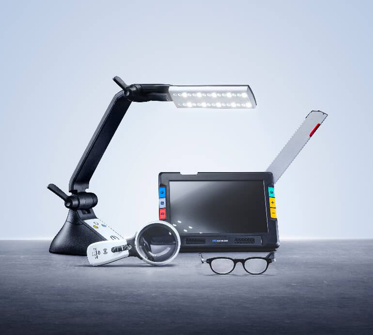 Schweizer Sehhilfen Low Vision Wollenhaupt Solingen Verschiedene moderne Low-Vision-Sehhilfen der Marke Schweizer auf grauem Untergrund arrangiert: Links eine verstellbare schwarze LED-Gelenkleuchte, daneben eine weiße Handlupe, mittig ein elektronisches Lesegerät mit Bildschirm und farbigen Bedientasten sowie im Vordergrund eine filigrane Lupenbrille.