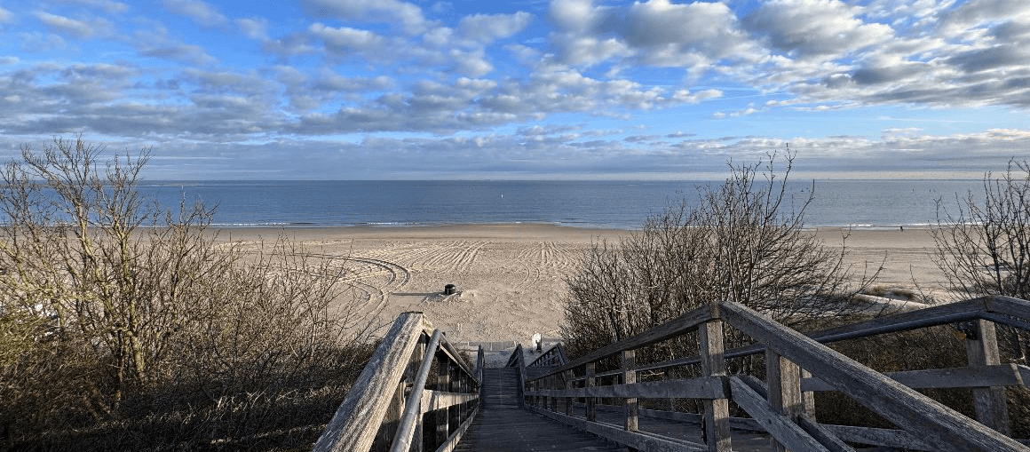 Vision und Werte Wollenhaupt Solingen Eine Holztreppe führt zu einem Strand am Meer mit blauem Himmel